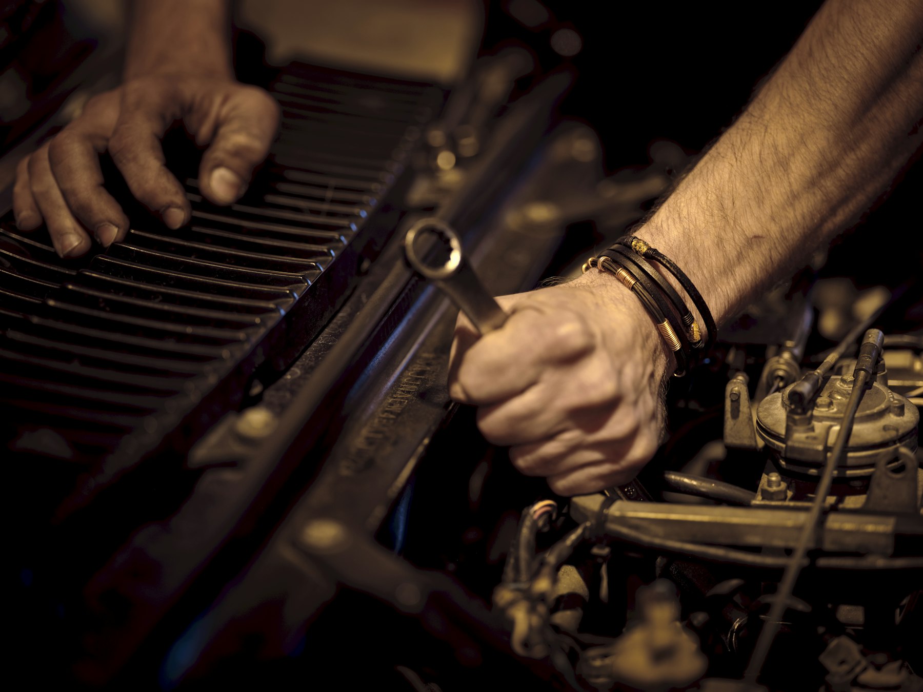 Hands turning a wrench in an engine bay.