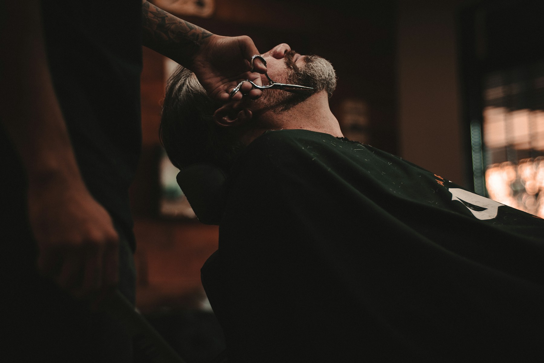 A beard being trimmed in a dark shop.